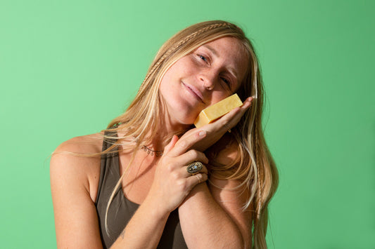 Smiling woman holding unscented natural soap bar against cheek, promoting eco-friendly and sustainable products on green background