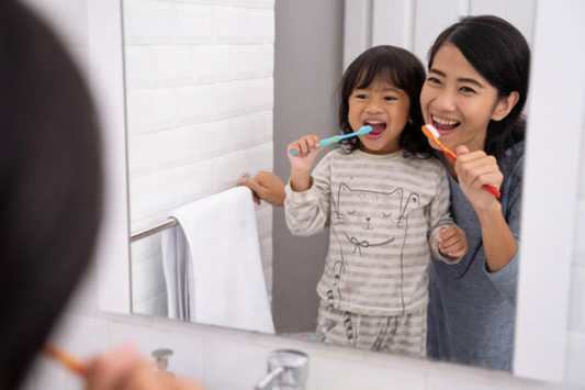Mom teaching daughter how to brush her teeth in bathroom