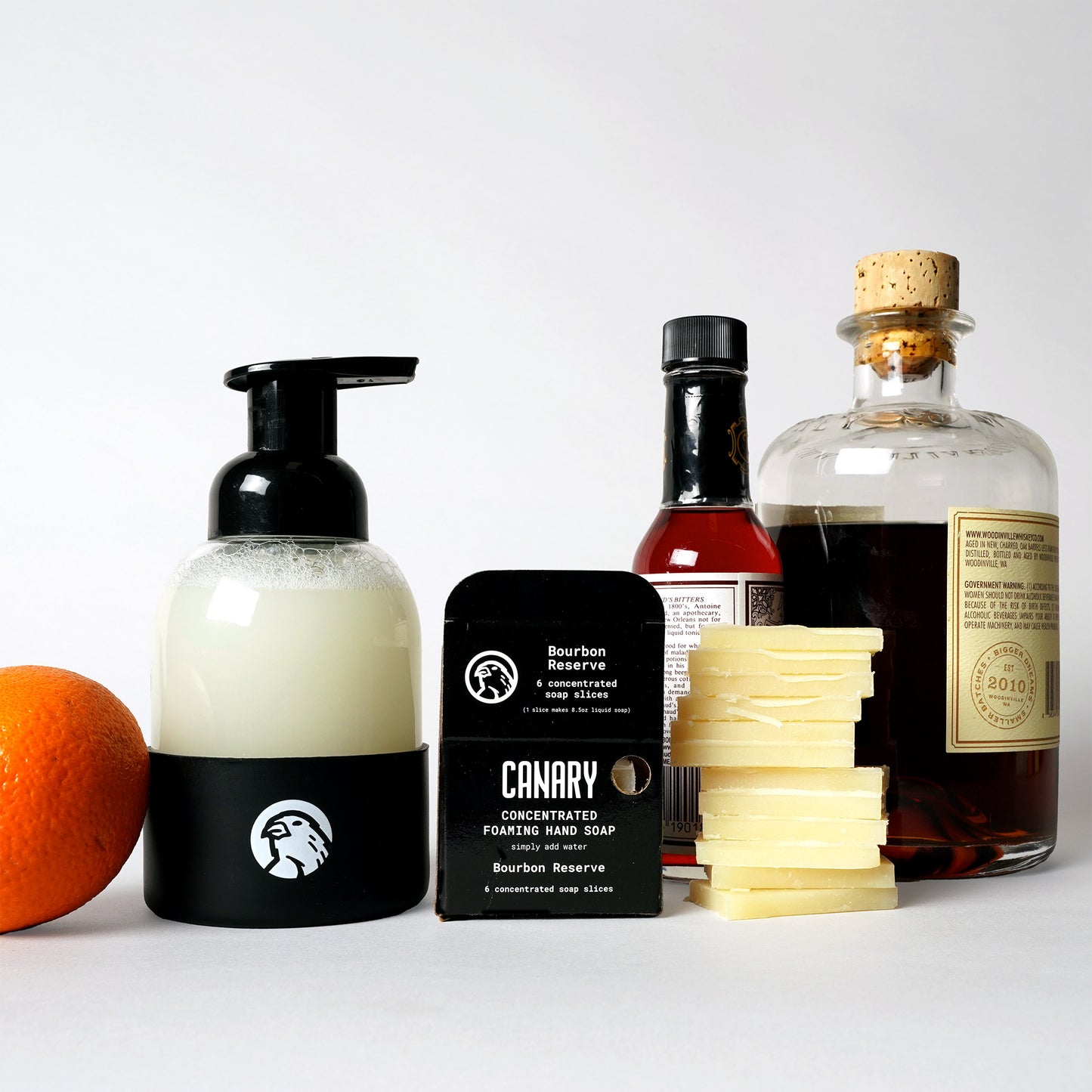 Image of Bourbon Reserve Foaming Hand Soap. 6 soap slices count. Sustainable refillable glass bottle filled with soap and 12 soap slices next to product. With bourbon and orange next to products.