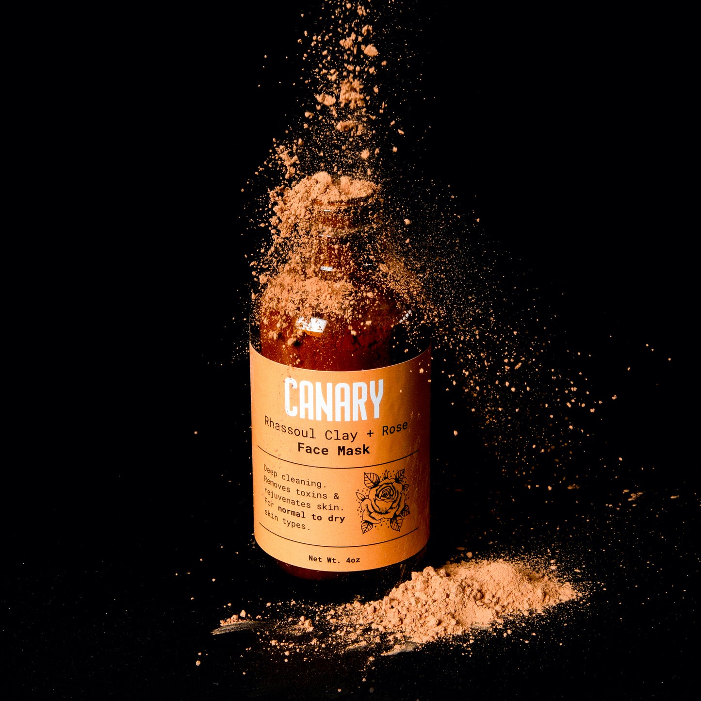 Rhassoul clay + rose face mask with powder dropping from above and around it. Eco-friendly, Vegan, and Plastic-Free