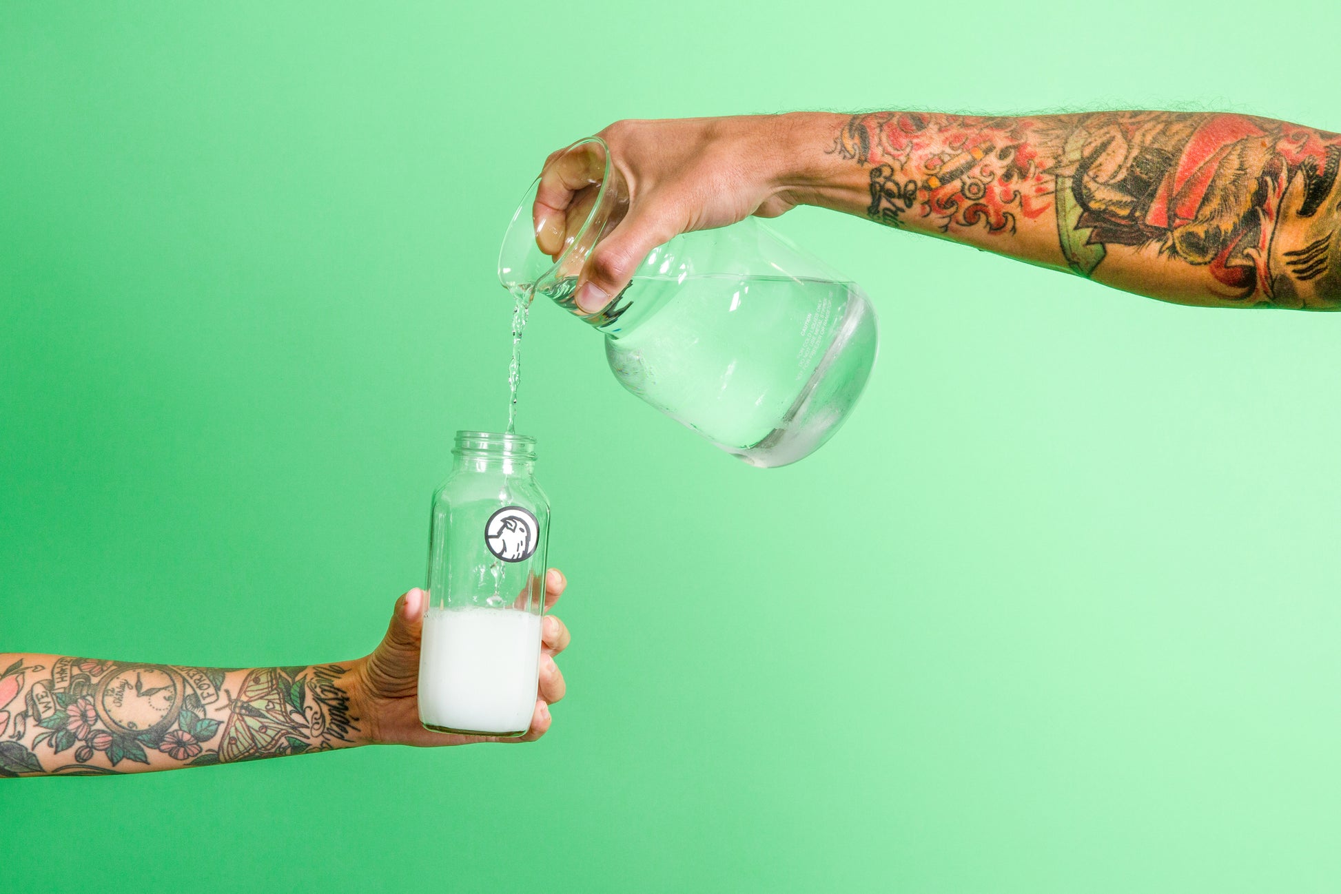 Hands pouring water into a reusable glass mixing bottle containing Canary Peppermint Mouthwash Concentrate