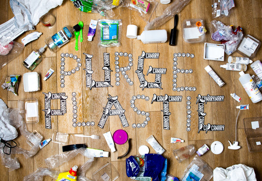 An array of plastic trash spread out on the floor with the words PURGE PLASTIC in the middle spelled out with Canary stickers