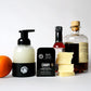 Image of Bourbon Reserve Foaming Hand Soap. 6 soap slices count. Sustainable refillable glass bottle filled with soap and 12 soap slices next to product. With bourbon and orange next to products.