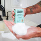 Fir Needle & Sage Concentrated Foaming Hand Soap. Front of the box with hands in sink showing how much foam there is. 12-count box. 