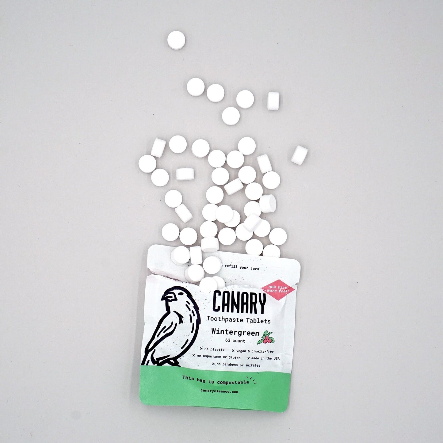 Canary Wintergreen Toothpaste Tablets, sample size 63 count compostable pouch, front view of the pouch with tablets spilling out of open pouch