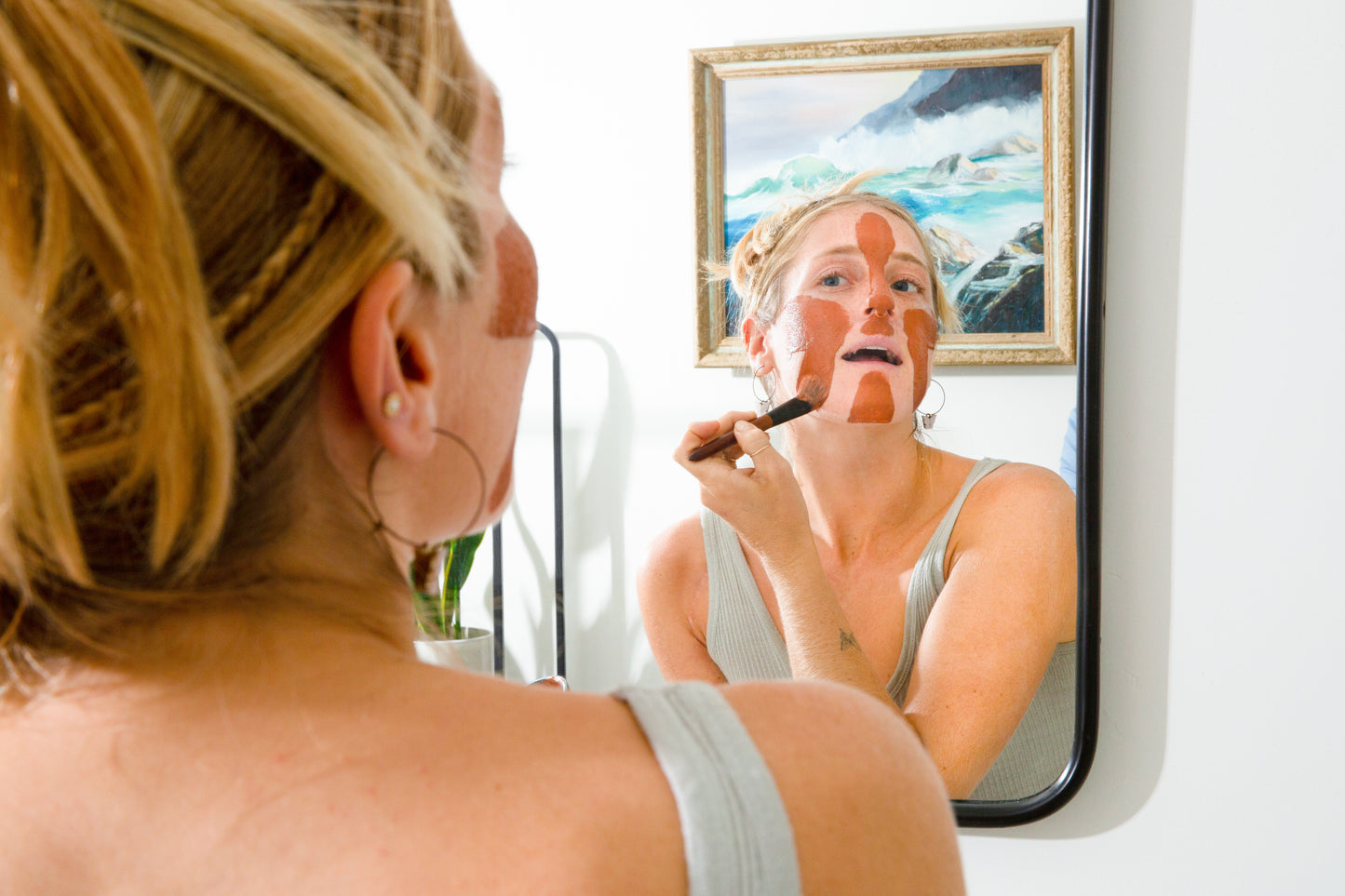 Tori applying Canary Rhassoul Clay + Rose Face Mask to her face with a facial brush while looking in the mirror