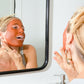 Tori with Canary Rhassoul Clay + Rose Face Mask applied on her face, smiling in the mirror