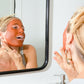 Tori with Canary Rhassoul Clay + Rose Face Mask applied on her face, smiling in the mirror