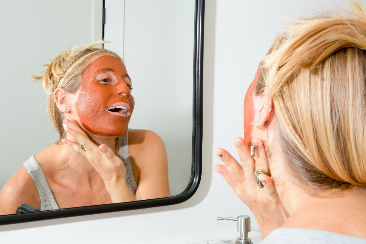 Tori with Canary Rhassoul Clay + Rose Face Mask applied on her face, smiling in the mirror