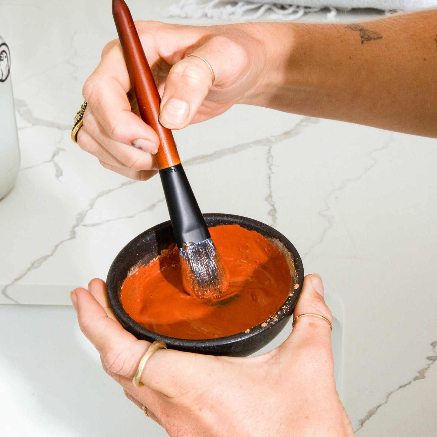 Closeup of Canary Rhassoul Clay + Rose Face Mask being mixed with water using a facial brush in a small bowl